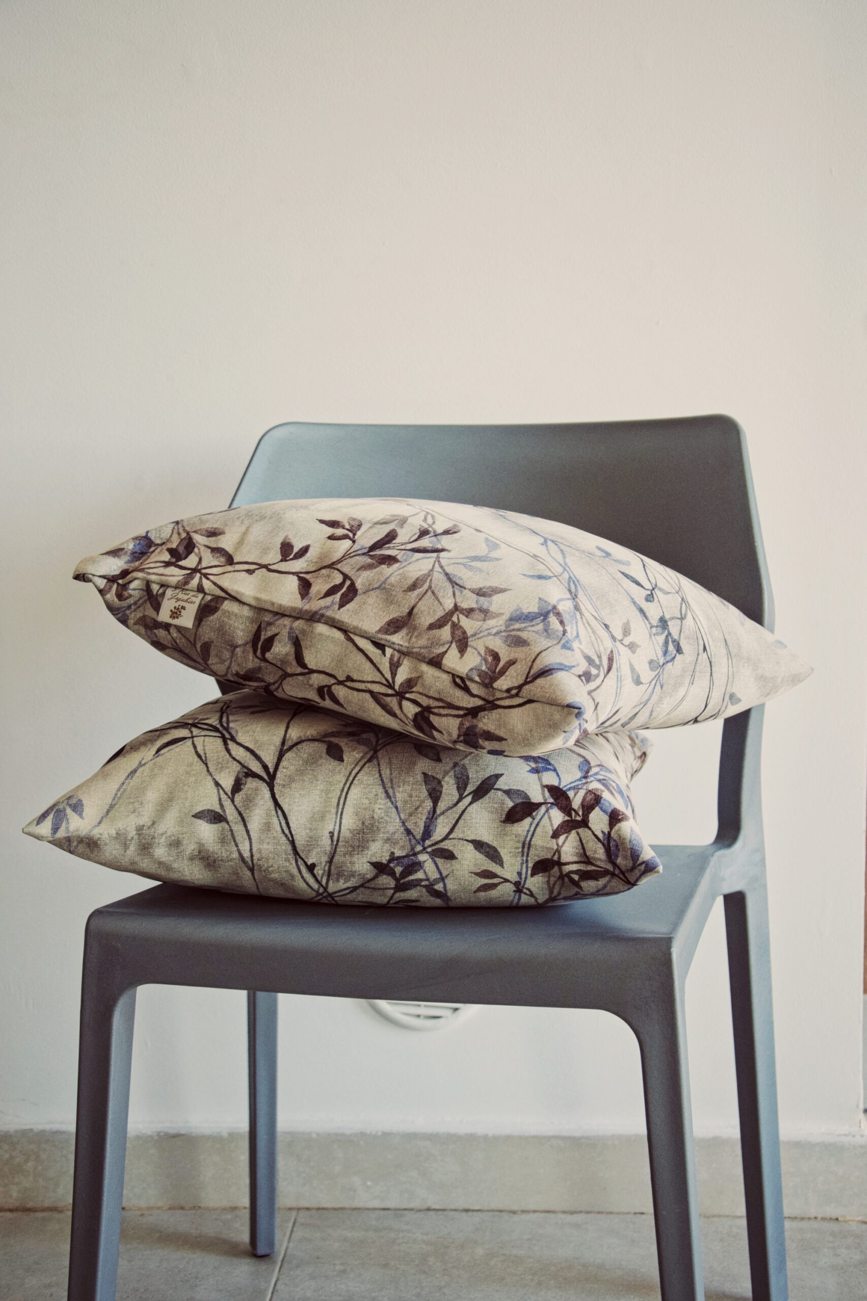 Coussin imprimé feuillage Percussion végétale, motif botanique bleu et bordeaux, empilé sur une chaise grise