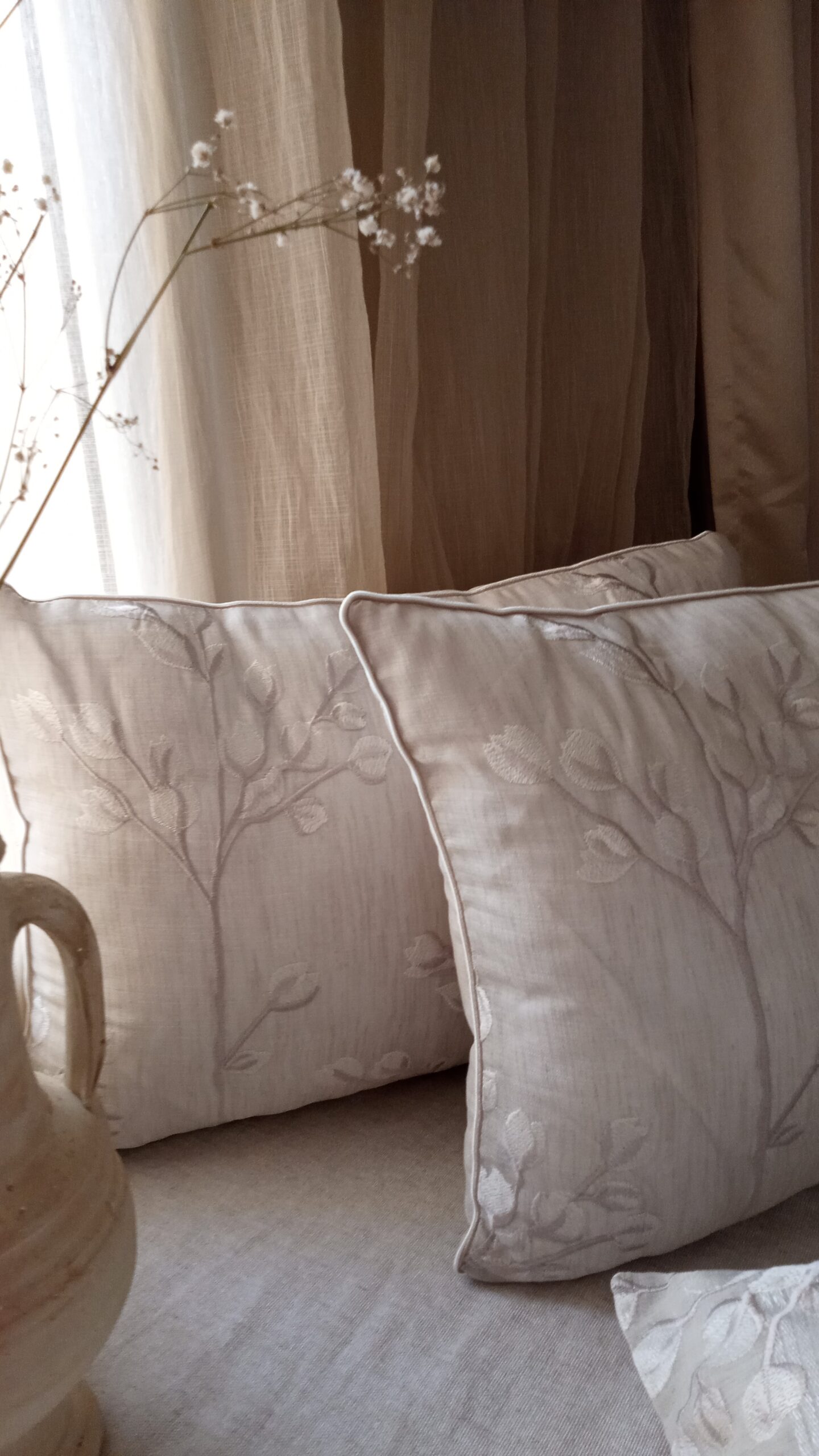 Coussin décoratif Jardin secret avec broderie florale sur fond beige, posé sur un lit dans une ambiance naturelle